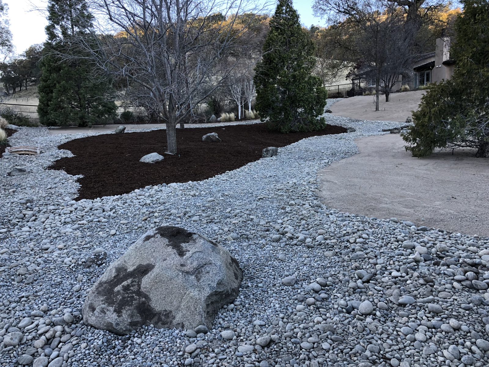 Dry creek bed with river rock and mulched tree beds