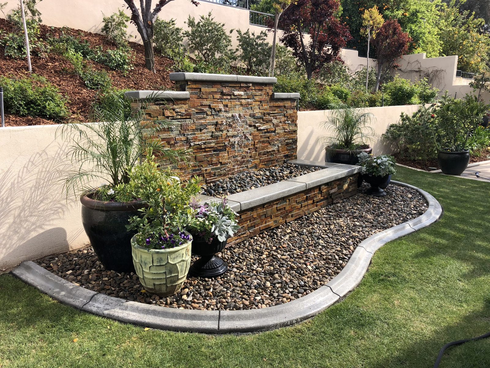 Stacked stone water feature with rock border and concrete curbing